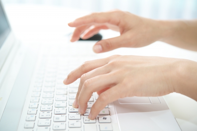 パソコンのキーボードを打つ女性の手の画像